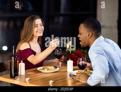 Allegra coppia interracial che si diverte a cena al ristorante, donna che alimenta il ragazzo Foto Stock