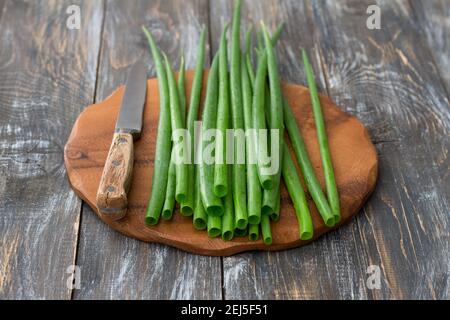 Cipolle biologiche verdi fresche e un coltello su una superficie di legno, fuoco selettivo Foto Stock