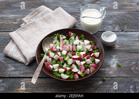 Insalata di rafano fresco con cipolle verdi e panna acida su fondo di legno, stile rustico. Deliziosi piatti fatti in casa Foto Stock