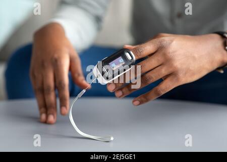 Uomo africano irriconoscibile che usa il pulsossimetro che verifica la saturazione dell'ossigeno in interni Foto Stock