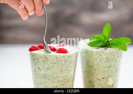 Bicchieri di frullato di banana al sedano con semi di chia, lamponi freschi e foglie di menta da vicino Foto Stock