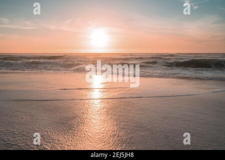 Tramonto sulla spiaggia. Luce del sole tenue giallo-rosa con bei riflessi del sole sulla sabbia dorata Foto Stock