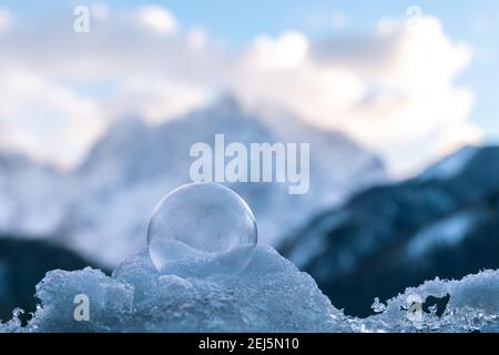 Belle bolle congelate seduti su un mucchio di neve e. ghiaccio con una delicata struttura di fiori di ghiaccio illuminati da il sole nascente con le montagne nel backgr Foto Stock