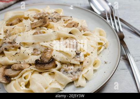 Elegante pasta di fetucine biologica con salsa cremosa di funghi alfredo. Superficie rustica. Foto Stock
