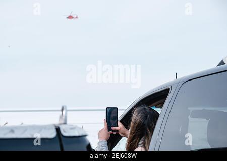 Cleveland, Ohio, Stati Uniti. 21 Feb 2021. Una donna fotografa un elicottero della Guardia Costiera degli Stati Uniti mentre le persone vengono salvate dal ghiaccio del lago Erie da membri della USCG Ice Rescue Team da Station Cleveland, così come da altre agenzie di soccorso locali, nel tardo pomeriggio di domenica, 21 febbraio 2021 a Edgewater Park a Cleveland, Ohio. Alle 12:43 EST, il Servizio meteorologico Nazionale a Cleveland emettere un avvertimento per non andare sul ghiaccio a causa dello sviluppo di crepe significative da venti meridionali. Secondo un Tweet dell'USCG Great Lake, la squadra di salvataggio del ghiaccio '''¦ USCG ha salvato 6 individui via il ghiaccio Foto Stock