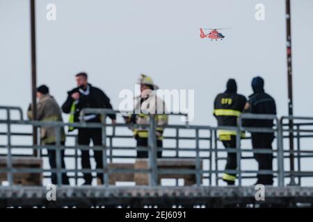 Cleveland, Ohio, Stati Uniti. 21 Feb 2021. Un elicottero della Guardia Costiera degli Stati Uniti sorvola il molo di Edgewater mentre le persone vengono salvate dal ghiaccio del lago Erie da membri della USCG Ice Rescue Team da Station Cleveland, così come da altre agenzie di soccorso locali, domenica pomeriggio tardi, 21 febbraio 2021 a Edgewater Park a Cleveland, Ohio. Alle 12:43 EST, il Servizio meteorologico Nazionale a Cleveland emettere un avvertimento per non andare sul ghiaccio a causa dello sviluppo di crepe significative da venti meridionali. Secondo un Tweet del Grande Lago USCG, il '''¦ USCG soccorso ghiaccio squadra ha salvato 6 individui vi Foto Stock