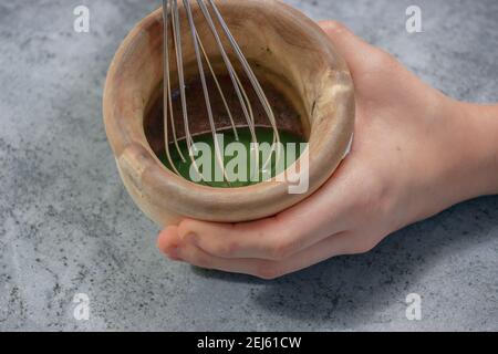 Immagine orizzontale della ciotola di argilla Matcha tè con zucchero, miele e acqua calda mescolato con un'asta di cucina su sfondo di pietra grigia. Concetto di tè verde giapponese Foto Stock