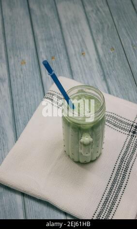 Immagine verticale Iced Matcha Tea su sfondo di legno blu con un mantellino. Concetto di tè verde giapponese. Preparazione del tè Matcha 2021. Foto Stock