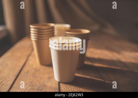 tazze monouso in carta marrone scuro e tazze bianche stare su un tavolo di legno su sfondo marrone Foto Stock