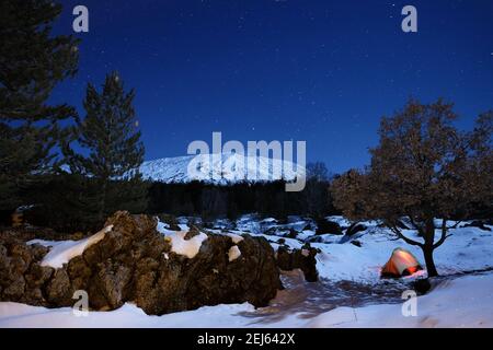 Formazione rocciosa 'ciara' e tenda luminosa nella neve del Parco dell'Etna sotto il cielo stellato, Sicilia Foto Stock