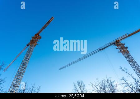 Molte gru a torre alta lavorano per la costruzione di nuove case. Due gru da costruzione contro il cielo blu. Vista delle due gru da costruzione Foto Stock