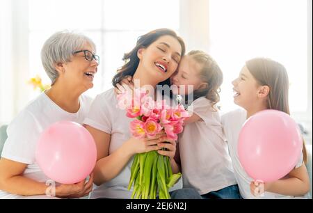Buon giorno delle donne! Le figlie dei bambini si congratulano con la mamma e la granata dando loro tulipani di fiori. Nonna, mamma e ragazze sorridenti e abbraccianti. Famiglia ho Foto Stock