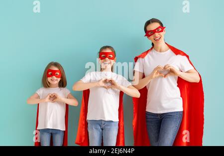 Madre e i suoi figli giocano insieme. Ragazze e mamma in costumi Superhero divertendosi e sorridendo. Vacanza in famiglia e insieme. Foto Stock