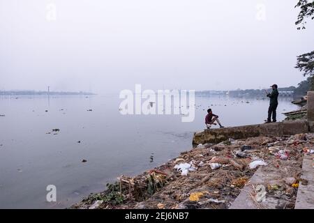 Kolkata, India. 21 Feb 2021. Gli uomini scattano foto alle rive inquinate del fiume Ganga. L'inquinamento idrico è uno dei maggiori problemi ambientali in India per varie ragioni. A Kolkata, ogni volta dopo ogni genere di pujas o festival religiosi, il fiume più santo, il Gange diventa terribilmente inquinato a causa del numero crescente di immersione idolo & spazzatura di leftover. Giorno dopo giorno il Gange sta perdendo la sua capacità di flusso e Kolkata, insieme ai suoi distretti circostanti, si trova a fronteggiare i peggiori problemi di alluvione ogni anno. Credit: SOPA Images Limited/Alamy Live News Foto Stock