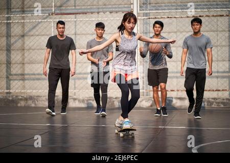 giovane donna asiatica skateboarder skateboarder all'aperto con amici che guardano da dietro Foto Stock