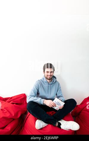 Duesseldorf, Germania. 19 Feb 2021. Tim Nießner, studente e autore di Best seller, si siede su una beanbag con il suo nuovo libro 'Der Zeugnisretter'. Nießner di Haan vicino Düsseldorf ha studiato sistematicamente le strategie dei migliori studenti tedeschi. Nel suo libro ha così una quantità di Tipps per gli allievi difettosi. (To dpa 'Operation Zeugnisrettung: Wie schlechte Schüler die Kurve kriegen') Credit: Fabian Strauch/dpa/Alamy Live News Foto Stock