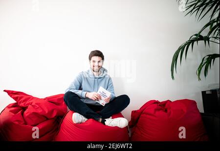 Duesseldorf, Germania. 19 Feb 2021. Tim Nießner, studente e autore di Best seller, si siede su una beanbag con il suo nuovo libro 'Der Zeugnisretter'. Nießner di Haan vicino Düsseldorf ha studiato sistematicamente le strategie dei migliori studenti tedeschi. Nel suo libro ha così una quantità di Tipps per gli allievi difettosi. (To dpa 'Operation Zeugnisrettung: Wie schlechte Schüler die Kurve kriegen') Credit: Fabian Strauch/dpa/Alamy Live News Foto Stock