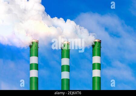 Tre tubi industriali di fumo da camino su cielo blu nuvoloso.il fumo bianco emana dai tubi. Foto Stock