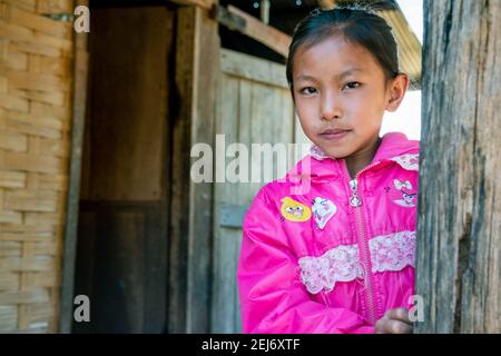 Ritratto di una giovane ragazza di villaggio asiatico in piedi presso l'ingresso della sua casa. Indossa una giacca rosa e guarda la fotocamera. Foto Stock