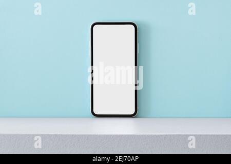 Telefono cellulare moderno con schermo vuoto posizionato sullo scaffale sfondo blu chiaro Foto Stock