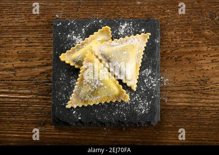 Ravioli freschi e triangolari ripieni crudi pasta italiana su A. tavola sgocciolata con farina vista in alto su un legno tabella Foto Stock