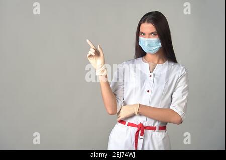 una dottoressa attenta in un abito medico, maschera e guanti, che avverte su qualcosa di importante. Foto Stock