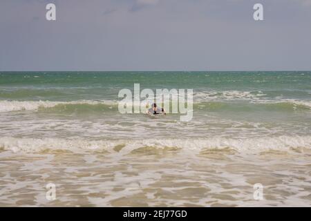 Giovani surfisti imparano a navigare in muta nera, giornata di sole sulla spiaggia dell'oceano Foto Stock