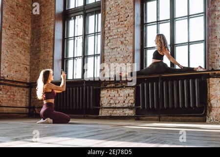 Due amici femminili scattano foto dopo un duro studio di stile loft di workout. Donna fare foto del suo amico flessibile facendo splits sul davanzale Foto Stock