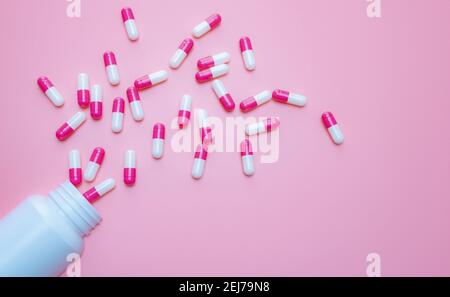 Capsule rosa-bianche la pillola è fuoriuscita dal contenitore del flacone di plastica su sfondo rosa. Resistenza agli antibiotici. Capsule antimicrobiche. Foto Stock