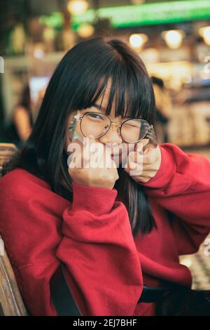 faccia divertente dell'adolescente asiatico solleva forchetta e cucchiaio sala da pranzo Foto Stock