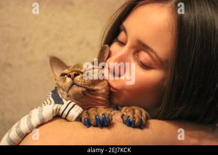 Una ragazza si abbracca e bacia il suo amato gatto della razza Sfinge canadese sulla guancia. Animali domestici adorati. Ritratto del gatto e della sua padrona. Silicone blu AN Foto Stock