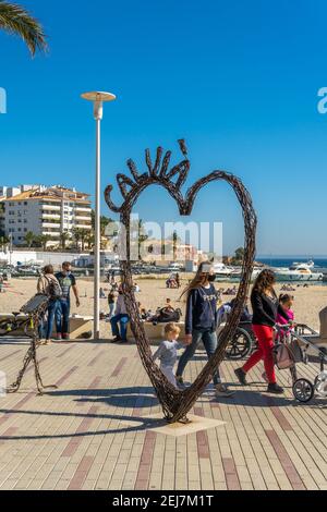 Palmanova, Spagna; febbraio 20 2021: Passeggiata marittima della località turistica maiorchina di Palmanova, con una scultura a cuore di ferro. Adolescenti a piedi Foto Stock