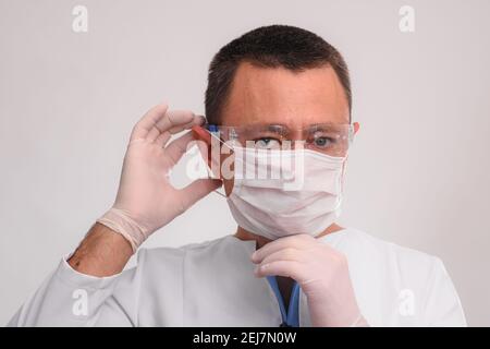 L'uomo indossa una maschera medica, occhiali e guanti protettivi. Su sfondo bianco. Foto Stock