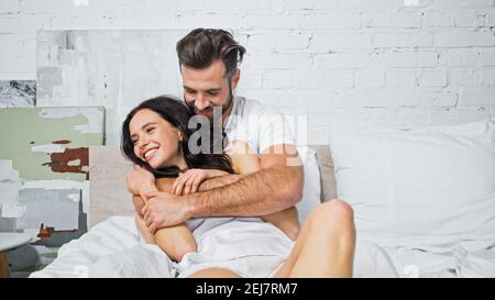 felice uomo abbracciando allegra donna brunette a letto Foto Stock