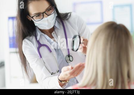 Medico che esamina la pelle sul viso del paziente utilizzando una lente di ingrandimento Foto Stock