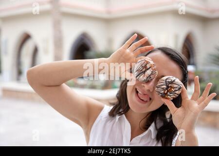 Ragazza divertente che posa con le ciambelle nelle sue mani in estate all'aperto. Concetto di vacanza. Foto Stock