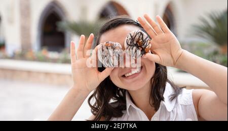 Ragazza divertente che posa con le ciambelle nelle sue mani in estate all'aperto. Concetto di vacanza. Foto Stock