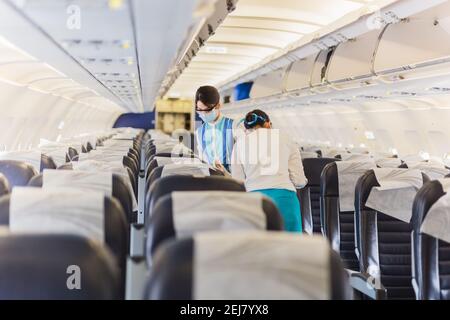 Assistente di volo in maschera facciale che controlla il sedile del passeggero. Foto Stock