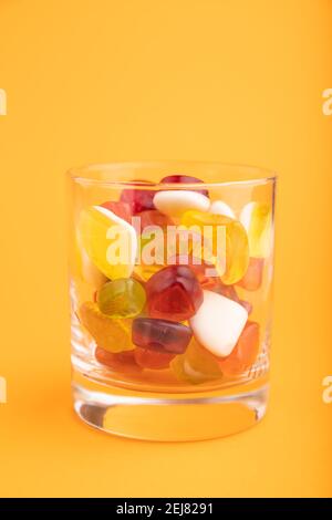 Varie caramelle di gelatina di frutta in vetro da bere su sfondo arancione pastello. Vista laterale, primo piano. Foto Stock
