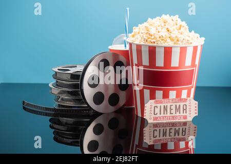 bobine di film, tazza di soda, biglietto per il cinema e secchio di popcorn su superficie lucida isolato su blu Foto Stock