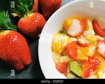 Ciotola di Macedonia di frutta fresca circondata da assortimenti di frutta fresca. Foto Stock