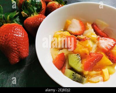 Ciotola di Macedonia di frutta fresca circondata da assortimenti di frutta fresca. Foto Stock