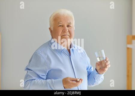 Uomo superiore positivo in camicia blu che tiene la pillola medica e. acqua pura in vetro nelle mani Foto Stock
