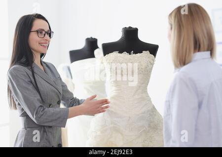 Consulente donna che mostra abito da sposa a sposa in salone Foto Stock