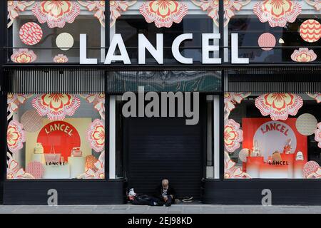 Uomo senza dimora fuori da un negozio di moda a parigi, francia Foto Stock