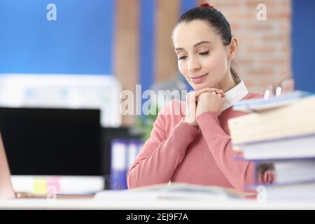 Giovane donna che legge libro e sorridendo in ufficio Foto Stock