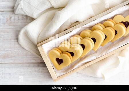 Biscotti a forma di cuore con confettura di lamponi e vaniglia in una scatola di legno con un tovagliolo bianco. Foto Stock