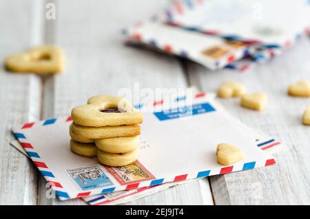 Biscotti a forma di cuore con confettura di lamponi e vaniglia su alcune lettere e su sfondo bianco di legno. Foto Stock