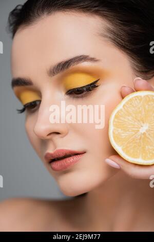 primo piano di giovane donna che tiene metà del limone maturo isolato su grigio Foto Stock