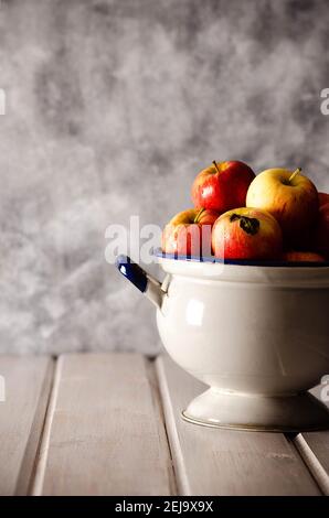 Mele rosse in un antico tureen, su uno sfondo bianco e grigio. Foto Stock